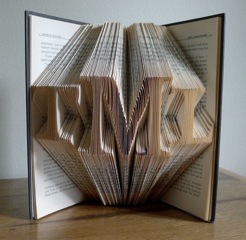 May include: A book art sculpture with the word "TIME" folded into the pages. The book is open and the pages are folded to create the letters. The book is on a wooden surface.