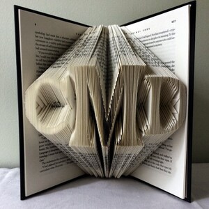 May include: A book with the letters "CMD" folded into the pages. The book is open and the pages are folded to create the letters.