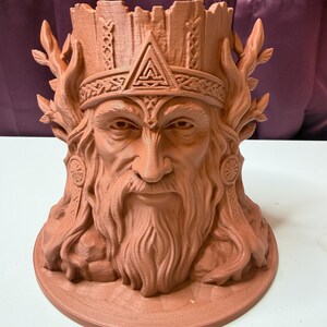 May include: A terracotta-colored planter shaped like a bearded figure wearing a crown. The figure features intricate facial details, a long beard, and tree-like branches extending from the sides. The top of the head forms a cylindrical opening.