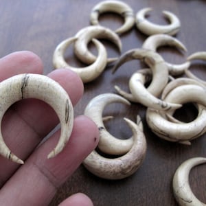 May include: A set of 12 wooden crescent moon shaped earrings. The earrings are made of light brown wood with dark brown streaks. The earrings are all different sizes and shapes.