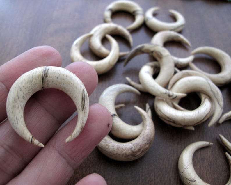 May include: A set of 12 wooden crescent moon shaped earrings. The earrings are made of light brown wood with dark brown streaks. The earrings are all different sizes and shapes.