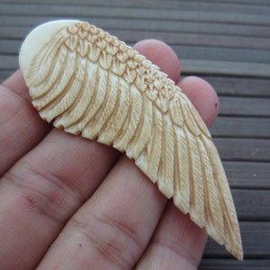 May include: A carved ivory wing pendant with detailed feather markings. The pendant is light brown in color and has a smooth, polished finish.