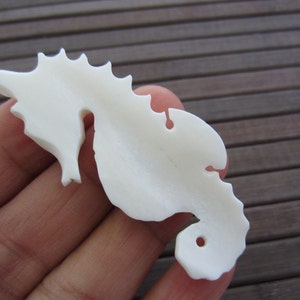 May include: White ceramic seahorse figurine with a detailed design. The figurine is smooth and has a hole in the bottom.