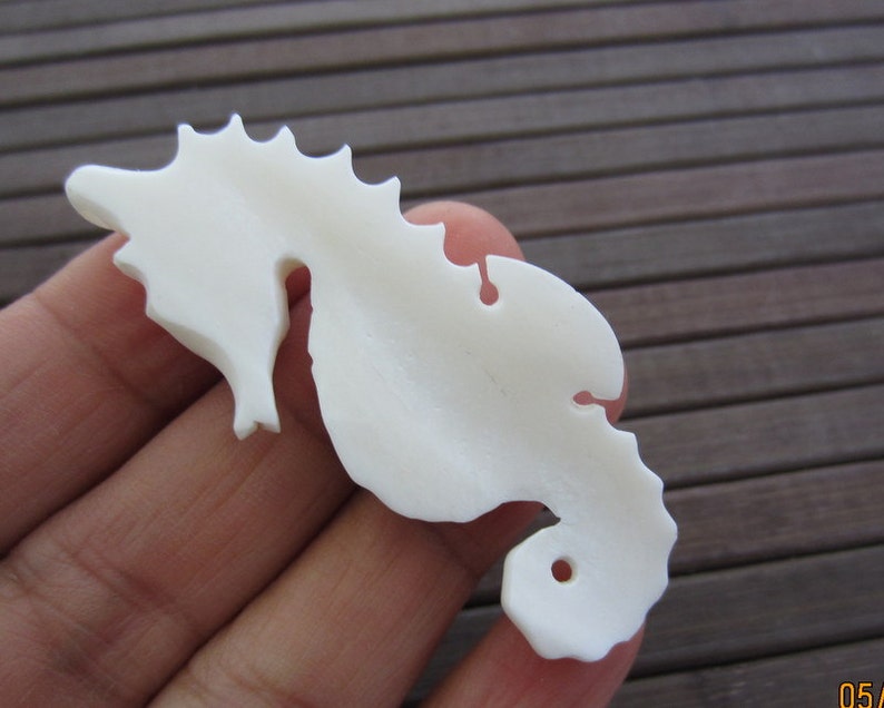 May include: White ceramic seahorse figurine with a detailed design. The figurine is smooth and has a hole in the bottom.