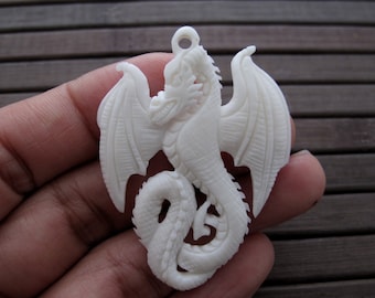 May include: White carved dragon pendant with wings outstretched. The dragon is intricately detailed and has a hole at the top for hanging.