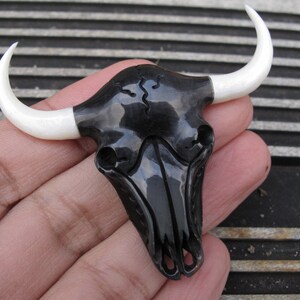 Può includere: Ciondolo a forma di teschio di toro nero e bianco con corna bianche. Il teschio è intagliato nel legno e ha una finitura lucida.