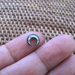 May include: A small crescent moon shaped earring made of abalone shell with a black metal backing.