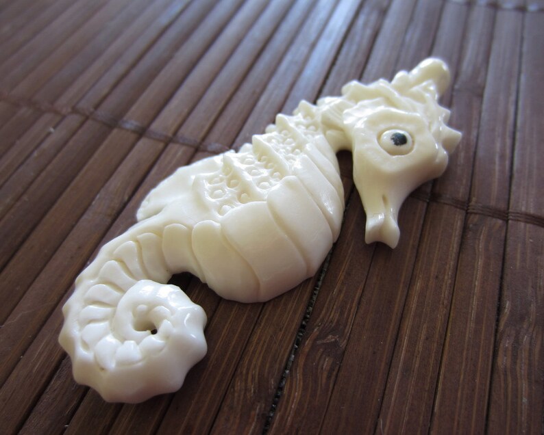 May include: A white carved seahorse figurine with a detailed design. The seahorse is lying on a brown bamboo mat.
