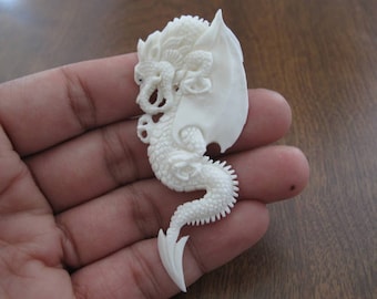 May include: A white carved dragon pendant with intricate details. The dragon is curled up with its wings spread out. The pendant is made of bone and is about 3 inches long.