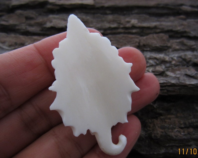May include: White ceramic leaf pendant with a detailed, intricate design. The leaf is smooth and has a slightly textured surface.