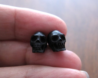 May include: Two black skull-shaped earrings. The skulls are detailed and have a matte finish.