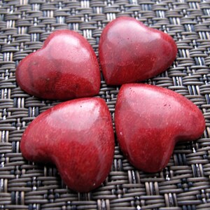 May include: Four red heart-shaped coral stones on a woven brown background.