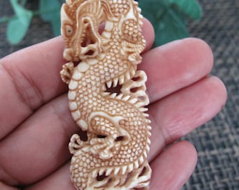 May include: A detailed, cream-colored dragon carving. The dragon is intricately carved with scales, claws, and a flowing mane. The carving is held in a hand, showcasing the detailed craftsmanship of the mythical creature.