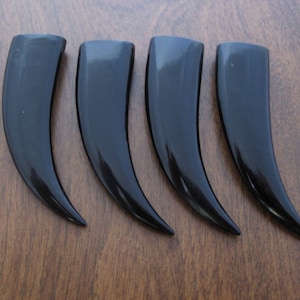 May include: Four black horn-shaped objects, possibly made of polished bone or plastic, are arranged in a row on a wooden surface.