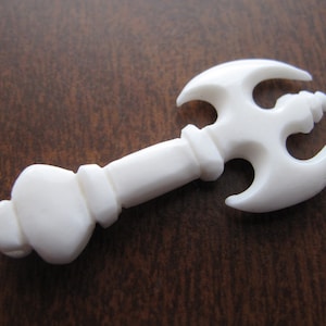 以下が含まれることがあります： 丸みを帯びたハンドルを持つスタイリッシュな斧の形をした、白く彫刻された骨のペンダント