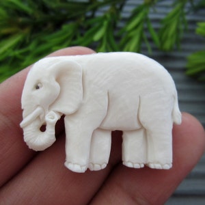 May include: A white carved elephant figurine made of bone. The elephant is standing with its trunk curled up.