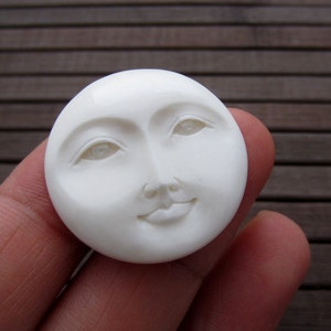 May include: White carved moon face pendant with a smiling expression and closed eyes.