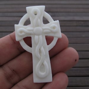 May include: White carved Celtic cross pendant with intricate knotwork design.