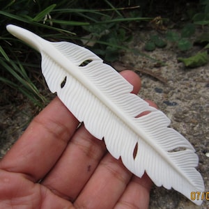 May include: A white carved bone feather with detailed lines and cutouts. The feather is about 6 inches long.