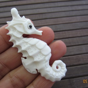 May include: A white carved seahorse figurine with detailed scales and a black eye. The figurine is made of bone and is approximately 3 inches tall.