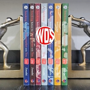 Könnte beinhalten: Ein Set aus sieben Manga-Bänden mit dem Titel Smoking Behind the Supermarket with You von Jinushi, mit nummerierten Buchrücken von eins bis sieben in verschiedenen Farben, gehalten zwischen zwei silberfarbenen Buchstützen in Menschenform.