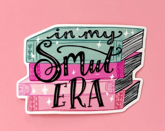 May include: A sticker featuring a stack of books with the text "in my smut era" written in black script. The books are pink, green and blue with white accents.