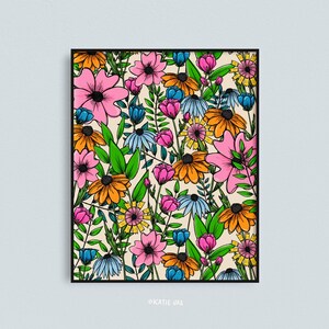May include: A framed floral art print featuring a vibrant array of colorful flowers. The artwork showcases pink, orange, blue, and yellow flowers with green leaves against a cream background. The print is in a black frame.