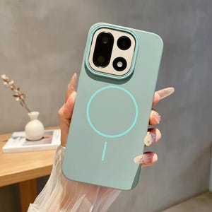 Könnte beinhalten: Eine hell mintgrüne Smartphone-Hülle mit quadratischem Kameraausschnitt für drei Linsen und einem kreisförmigen magnetischen Ladering auf der Rückseite. Die Hülle hat eine glatte, matte Oberfläche und einen vertikalen Strich als Akzent.