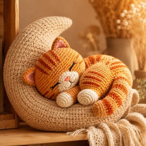 Può includere: Un gatto tigrato arancione all'uncinetto con zampe e muso bianchi dorme raggomitolato su un grande cuscino beige a forma di mezzaluna. Il gatto ha gli occhi chiusi, l'interno delle orecchie rosa e strisce arancione scuro sul corpo e la coda.
