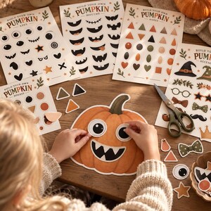 Op de afbeelding: Een set Build Your Own Pumpkin stickervellen met diverse ogen, monden, neuzen en accessoires in oranje, zwart en groen. De collectie bevat bedrukte papieren vellen, een grote papieren pompoenuitsparing en een metalen schaar.