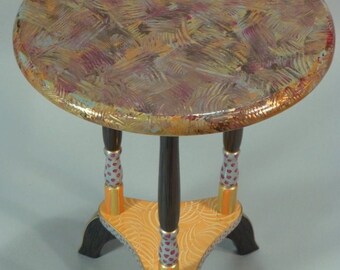 May include: A round, three-legged table with a colorful, abstract painted top. The table legs are painted with black, gold, and white polka dots.