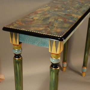 May include: A decorative console table with a blue and green painted top and black trim. The table has three legs with a green, black, and gold painted design.
