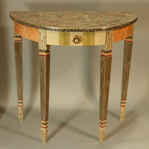 May include: A half-round table with a single drawer and three legs. The table is painted in a variety of colors, including orange, green, and gold. The legs are decorated with painted flowers.
