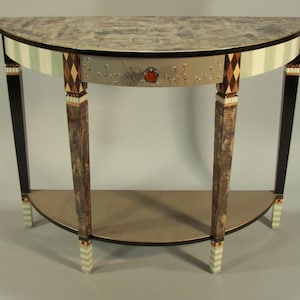 May include: A half-round table with a silver drawer and a decorative knob. The table has a black base with white and green painted stripes. The table top is a light brown with a marbled pattern.