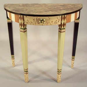 May include: A half-moon accent table with a painted floral design on the drawer and tabletop. The table features a drawer with a flower-shaped knob, and the legs are painted in alternating colors of black, cream, and light green.