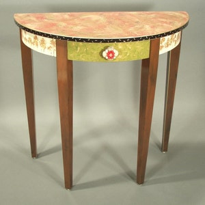 May include: A half-round table with a green drawer and a floral knob. The table top is painted with a marbled design in shades of pink and brown. The table legs are dark brown wood.