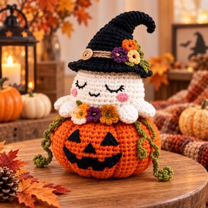 Peut inclure: Un fantôme au crochet portant un chapeau de sorcière noir avec un bouton en bois et des fleurs colorées, assis sur une citrouille d'Halloween orange au crochet avec un visage noir cousu et des vignes vertes, yeux fermés et joues roses.