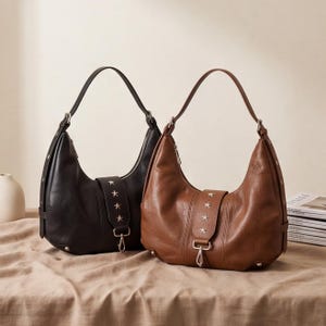 May include: Two hobo-style shoulder bags, one in black and one in brown, featuring a central vertical strap adorned with four silver-toned star studs and a metal clasp closure. Each bag has a single shoulder strap and silver-toned hardware accents.