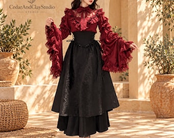 May include: A long-sleeved deep red blouse with lace trim and ruffled cuffs paired with a black high-waisted skirt featuring a corset-style lace-up front. The garment includes a matching red hair bow. Text reads C C CedarAndClayStudio.