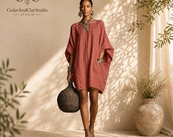 May include: A loose-fitting, knee-length dress in a muted terracotta colour with wide, short sleeves and a round neckline. The garment features a textured fabric, side pockets, and is paired with dark strappy sandals and a round woven dark bag.