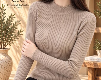 May include: A beige long-sleeve jumper featuring a ribbed knit texture, a mock neck collar, and scalloped edges at the cuffs and neckline. The garment displays a vertical ribbed pattern throughout the torso and sleeves, providing a fitted look.