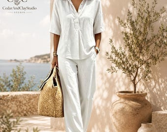 May include: A white collared shirt with short sleeves and a button-down placket paired with matching white wide-leg trousers. The outfit is worn with a large woven straw tote bag and brown sandals. The CedarAndClayStudio logo is visible.
