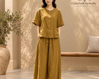 May include: A mustard yellow two-piece set consisting of a short-sleeved button-down shirt with a round neckline and two front pockets, paired with matching wide-leg trousers featuring a drawstring waist. The CedarAndClayStudio logo is visible.