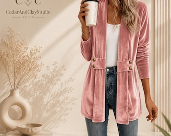May include: A dusty pink velvet blazer featuring a shawl collar, long sleeves, and a double-breasted front detail with four gold-toned buttons. The blazer is worn over a white top and blue denim jeans, with a white coffee cup held in one hand.