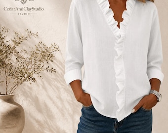 May include: A white long-sleeved blouse featuring a deep V-neckline adorned with vertical ruffles that extend down the front. The shirt has cuffed sleeves and is paired with dark blue denim jeans. A silver-toned wristwatch is worn on the wrist.
