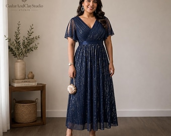 May include: A navy blue midi dress featuring a V-neckline, short split flutter sleeves, and a pleated skirt with vertical metallic silver pinstripes. The dress has a fitted waistline and is paired with a small gold shell-shaped clutch purse.