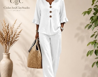 May include: A white two-piece set consisting of a V-neck top with three brown buttons and ruffled three-quarter length sleeves, paired with matching wide-leg trousers. The top features a central vertical seam and a relaxed fit throughout.