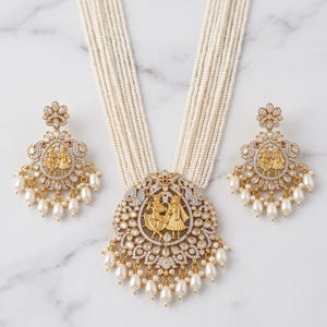 May include: A multi-strand white seed bead necklace featuring a large circular gold-tone pendant with a central embossed figure motif, surrounded by clear stones and dangling white pearls, paired with matching circular drop earrings.