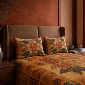 Puede incluir: Dos almohadas rectangulares y una colcha con un diseño de patchwork en tonos óxido, dorado y azul cerceta oscuro. La tela muestra intrincados patrones florales y geométricos dispuestos en un motivo repetitivo de estrellas y bloques.