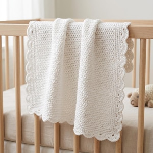 Può includere: Una coperta all'uncinetto bianca caratterizzata da un motivo a punti denso e uniforme al centro e da un bordo decorativo smerlato. Il tessuto è drappeggiato sulla sponda di una culla in legno, mettendo in risalto la lavorazione del filato.